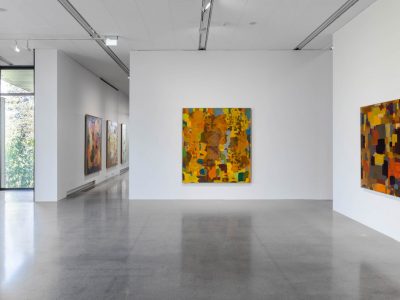 Om Artipelags galleriinteriör visar upp ett betonggolv och vita väggar prydda med stora, levande abstrakta målningar. Naturligt ljus filtreras genom ett fönster till vänster och förstärker den konstnärliga atmosfären.