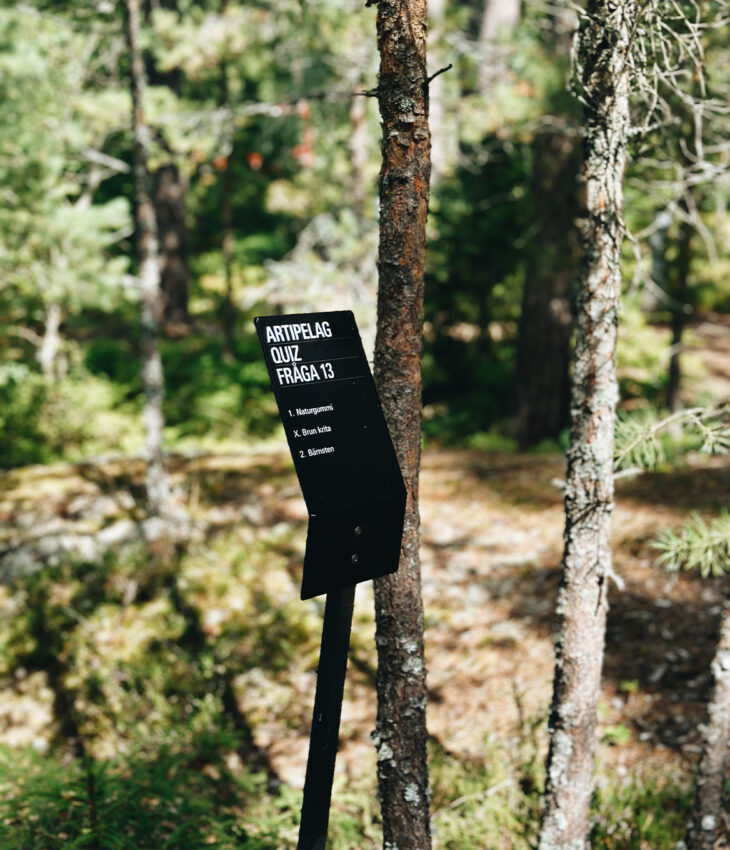 Bilden föreställer en skylt med en fråga från Artipelags tipspromenad. I bakgrunden skymtar skog.