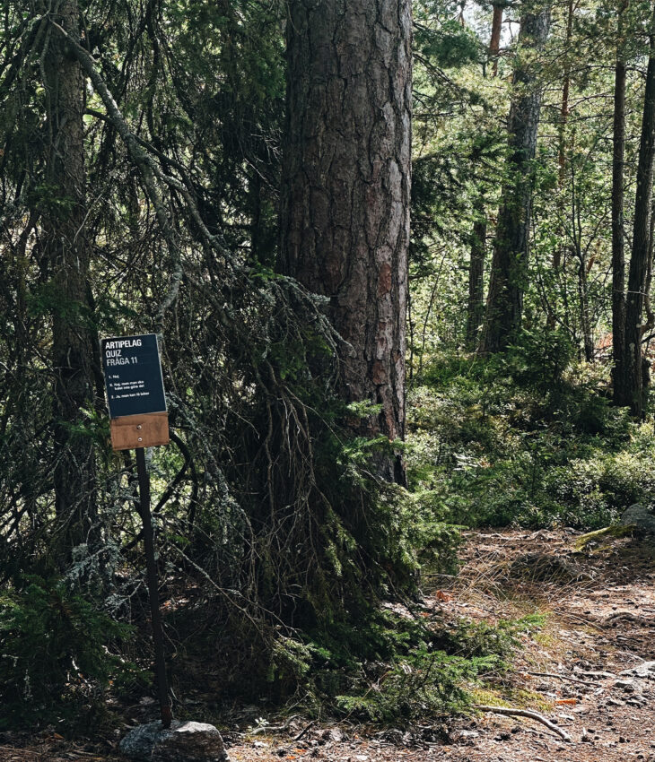 Bilden föreställer en skylt med en fråga från Artipelags tipspromenad. I bakgrunden skymtar skog.