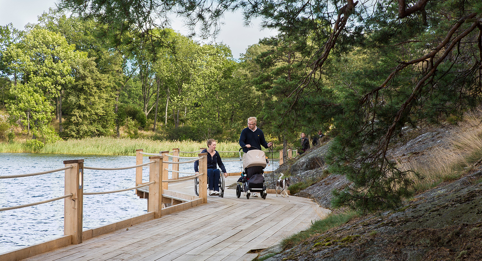 Kvinna i rullstol och man med barnvagn färdas på Artipelags strandpromenad.