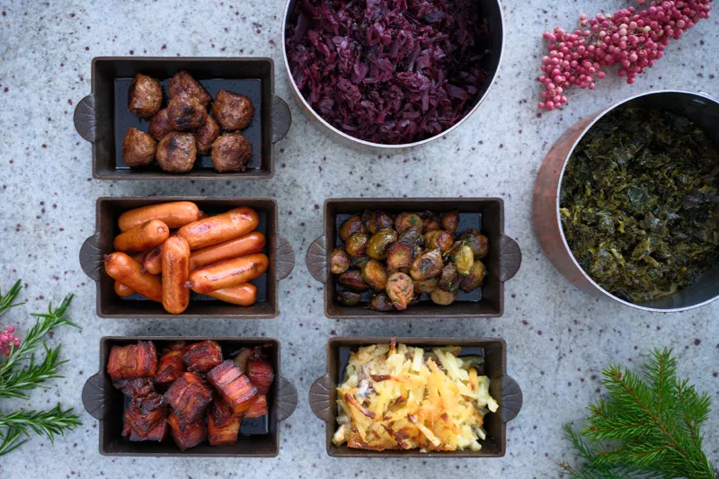 Bilden föreställer ett dukat julbord med varma rätter så som Janssons frestelse, rödkål, prinskorvar, köttbullar och revbensspjäll.