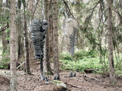 Bild på konstnären Annika Liljedahls skulptur placerad i en skogsglänta. Skulpturen föreställer två kokonger uppspända med fiskelina mellan tallstammarna.