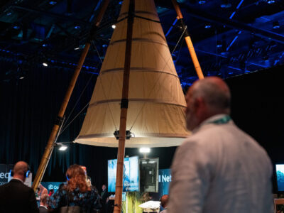 Deltagarna samlas runt en stor, upplyst, konisk tältliknande struktur inne i det svagt upplysta evenemangsutrymmet och surrar av spänning inför Arrow Innovation Awards 2024.